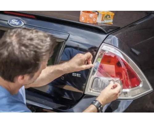 En person reparerar en baklykta på en bil med Gorilla tejp