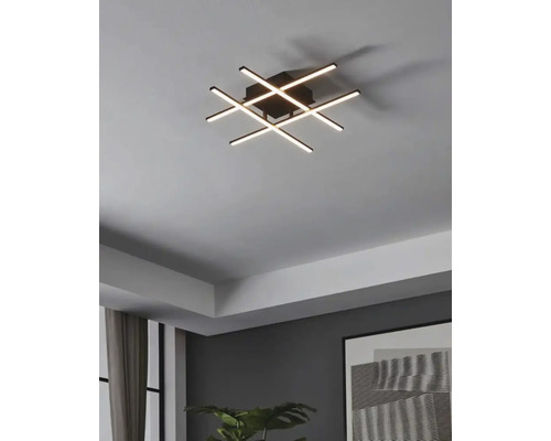 Modern taklampa med korsande LED-ljusstavar i ett vardagsrum.