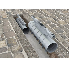 Installerade dräneringsrännor med rör och galler i en stenlagd väg.