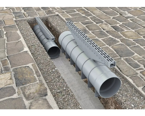 Installerade dräneringsrännor med rör och galler i en stenlagd väg.