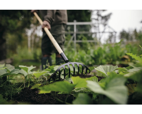 Trädgårdsscen med person och en kultivator för att luckra upp jorden
