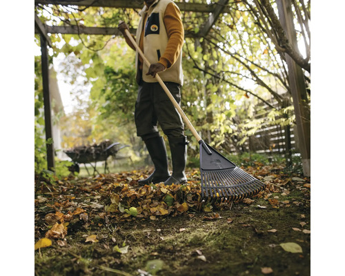 En person krattar löv med en lövgrep i trädgården.