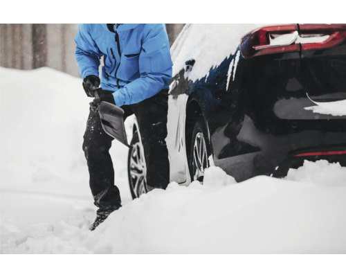 Person som skottar snö bredvid en bil.