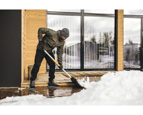 En person skottar snö framför ett hus med en snöskyffel.