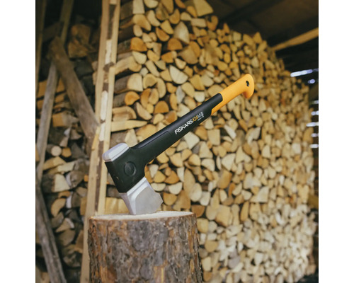 Fiskars klyvyxa på en huggkubbe framför en stapel med trä