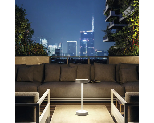 Modern terrassdesign med loungemöbler och trådlös bordslampa med nattligt stadslandskap i bakgrunden.