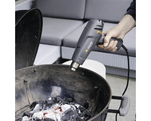 En person tänder grillkol med en Steinel varmluftspistol.