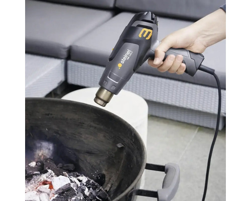 En person tänder grillkol i en grill med en varmluftspistol.