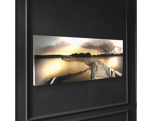 Väggbild med en träbro över en sjö i solnedgången