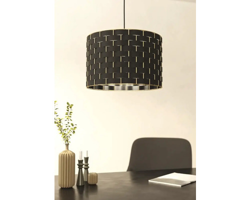 Hänglampa med svart lampskärm och flätat mönster över ett matbord.