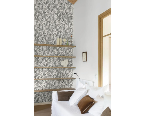 Vardagsrum med mönstrad tapet, trähyllor och vit soffa.