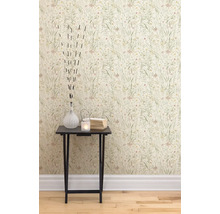 En närbild av en vägg med blomstertapet och ett sidobord med dekorativa föremål som en vas, ett värmeljus och böcker.