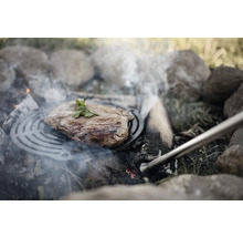 Stek på grillgaller över öppen eldstad med stenar.