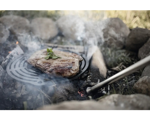 Stek på grillgaller över öppen eldstad med stenar.