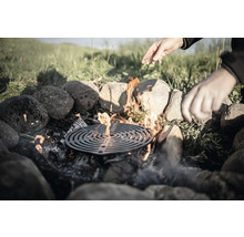 Eldstad med grillgaller, omgiven av stenar, med händer ovanför