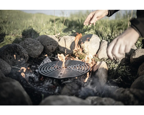 Eldstad med grillgaller, omgiven av stenar, med händer ovanför
