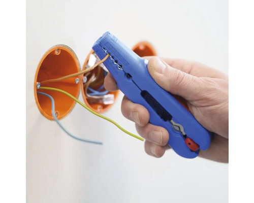 En person använder en avisoleringstång för att skala en kabel. Två orangefärgade kopplingsdosor syns i bakgrunden.