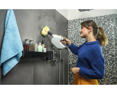 Kvinna rengör badrumsplattor med ångtvätt. Hygienartiklar står på hyllan.