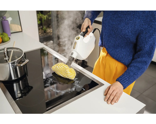 En person rengör en spishäll med en ångrengörare och en trasa.