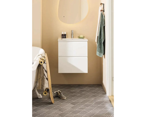 Ljust badrum med vitt tvättställsskåp, spegel och mönstrade golvplattor