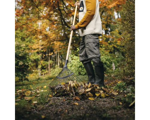 Person som krattar löv med en lövräfsa i trädgården.