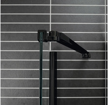 Detaljvy av en duschkabin med glas och svart ram mot en kaklad vägg
