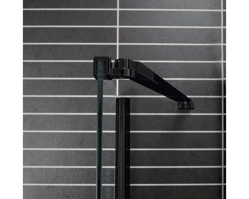 Detaljvy av en duschkabin med glas och svart ram mot en kaklad vägg