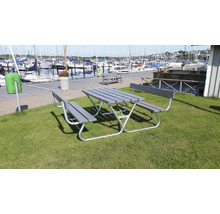 Grå picknickbordsuppsättning med bänkar på en gräsmatta nära en hamn.