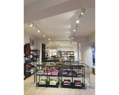 Interiör av en klädaffär med hyllor fulla av vikta kläder och en rad spotlights i taket.
