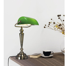 Grön skrivbordslampa i bankstil på ett träbord med bok, kopp och blomvas.