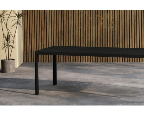 Svart trädgårdsbord i aluminium framför en vägg med träpanel och en krukväxt.