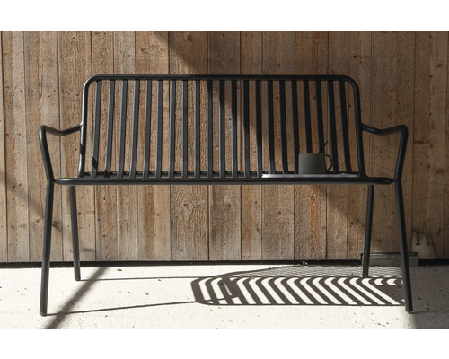 Trädgårdsbänk i metall med kopp och bok framför trävägg