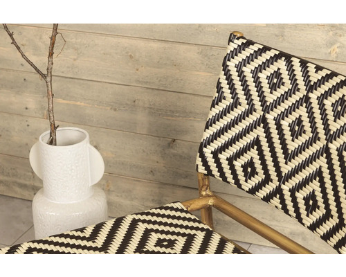 Detaljbild av en rottingstol med geometriskt mönster och en vit vas med en kvist