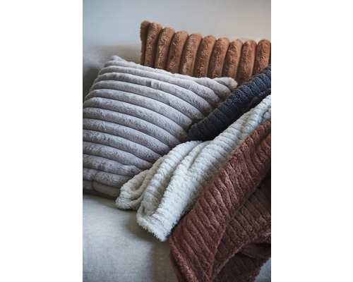 Olika kuddar och filtar med ribbad struktur på en soffa