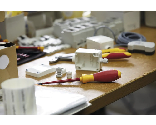 Bild av elektrikerverktyg och material på en arbetsbänk, inklusive skruvmejslar, höljen och kabelförskruvningar