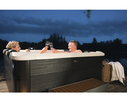 Två personer skålar i en bubbelpool med champagneglas. Bubbelpoolen står utomhus på en träterrass.