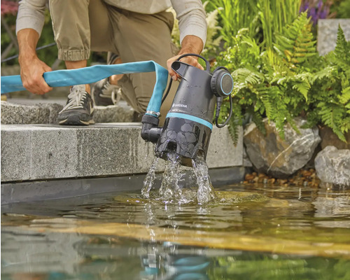 En person tömmer en trädgårdsdamm med en Gardena pump och slang.