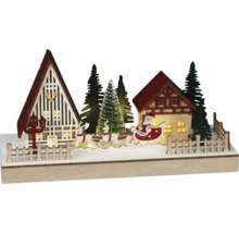 Belyst juldekoration med hus, julgranar och jultomten i en släde