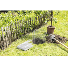 Trädgårdsscen med staket, spade, trådnät och träd i kruka