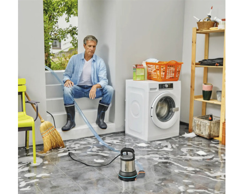 Man sitter på trappan och använder dränkbar pump för att avlägsna vatten i rummet