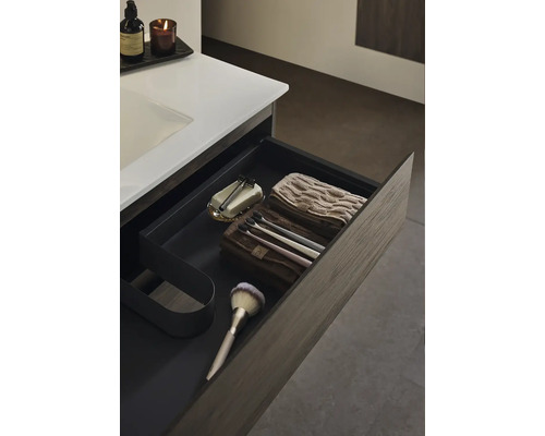 Öppen låda i badrum med rakhyvel, tvål, handdukar, tandborstar och borste