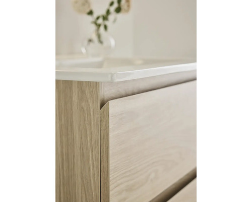 Detaljbild av ett tvättställsskåp med lådor och keramisk tvättställ