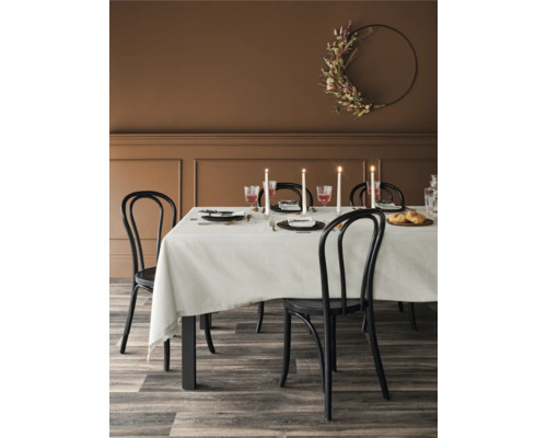 Matbord med dukning, stolar och en blommig krans på väggen i en matsal.