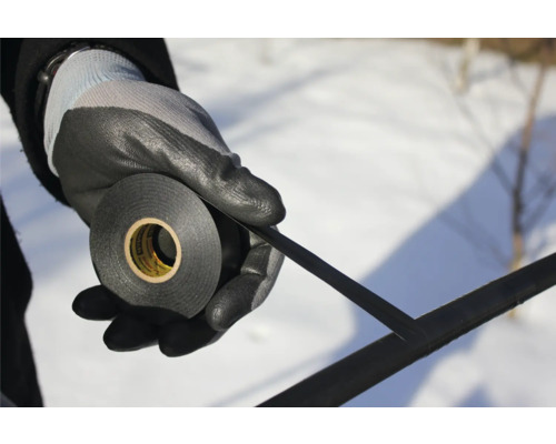 En person håller en rulle isoleringstejp med arbetshandskar.