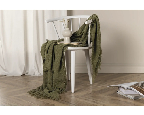 Dekorativ scen med en grön pläd över en vit stol, en vas och böcker