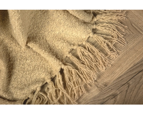 Beige överkast med fransar på trägolv