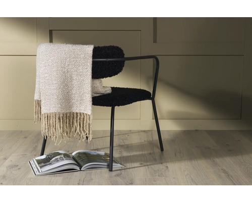 Dekorativt arrangemang med stol, filt och tidskrift för mysig rumsdesign.