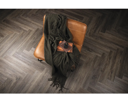 Fåtölj med filt, böcker och ljus på ett fiskbensparkettgolv