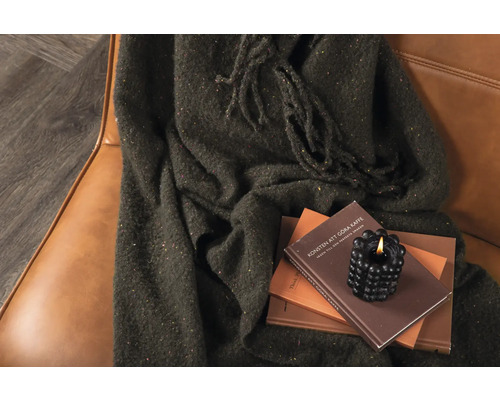 Dekorativ scen med filt, böcker och ljus på en fåtölj