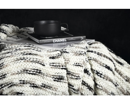 Dekorativ scen med en stickad filt, en bok och en kopp